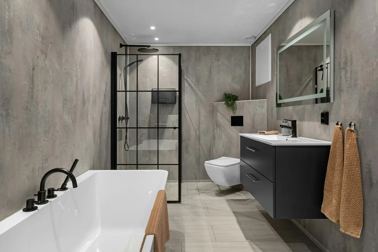 Grey-tiled bathroom with black taps, a crittall-style shower screen and wall-hung toilet
