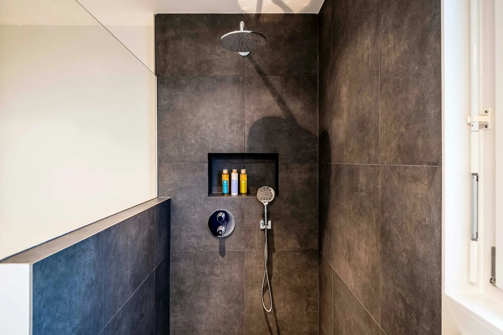 Walk-in shower with dark tiles, a niche and a handheld shower