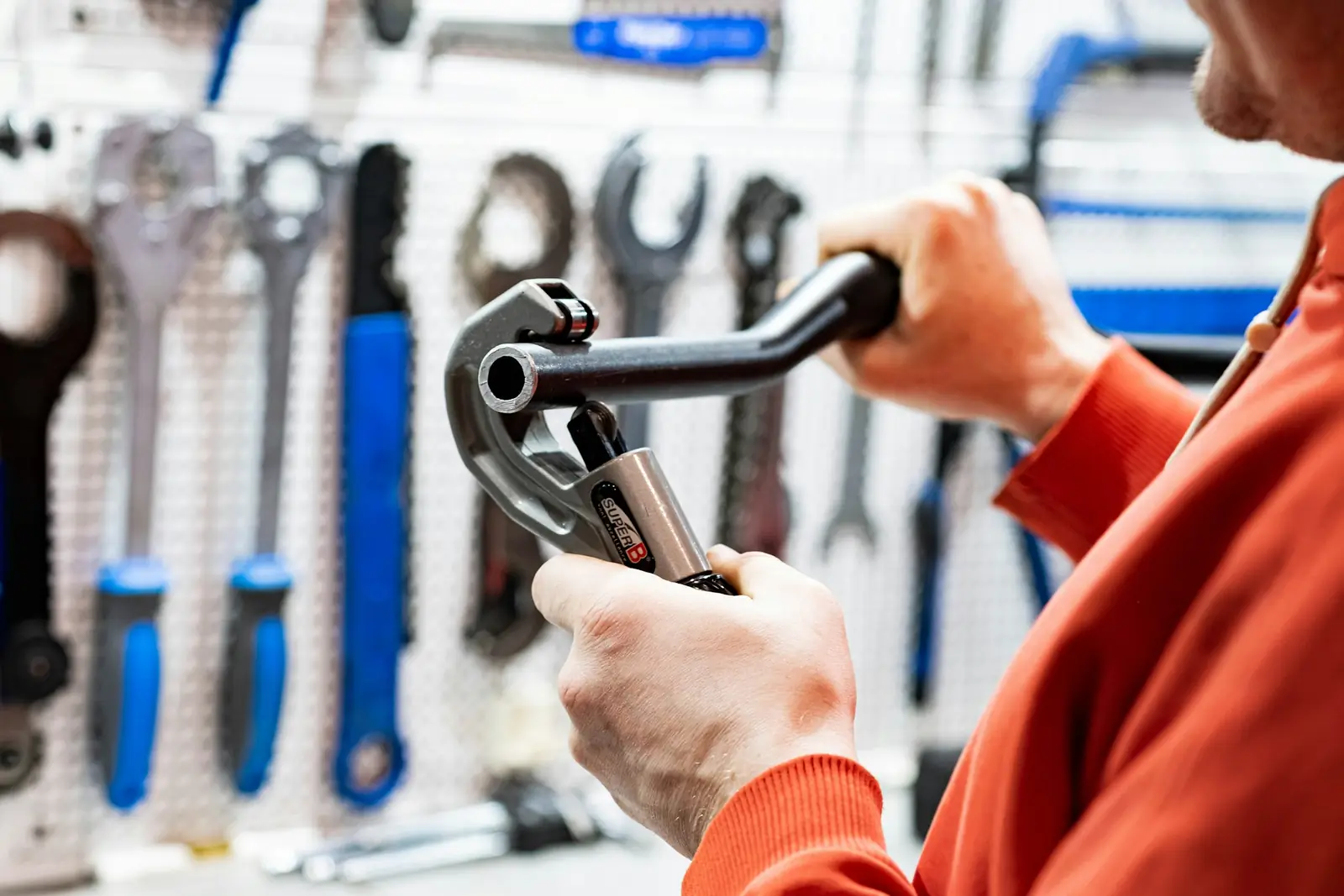 Plumber holding a pipe wrench in front of a wall of hand tools