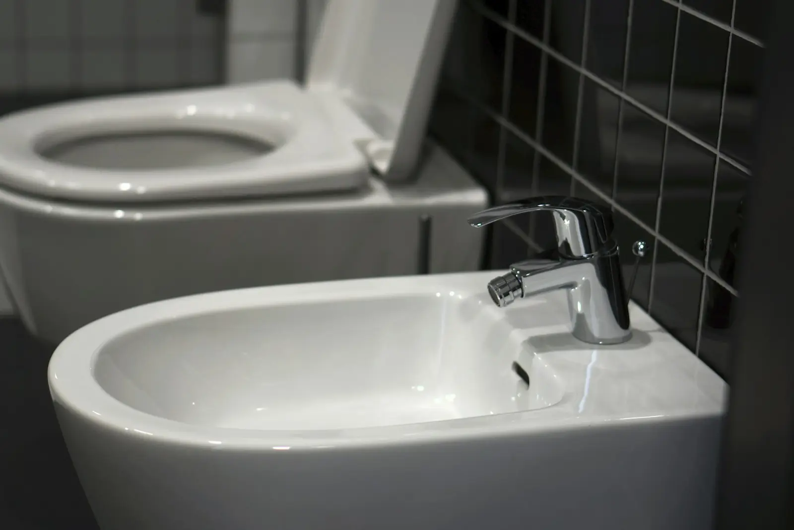 Toilet and bidet with a chrome mixer tap in a tiled bathroom