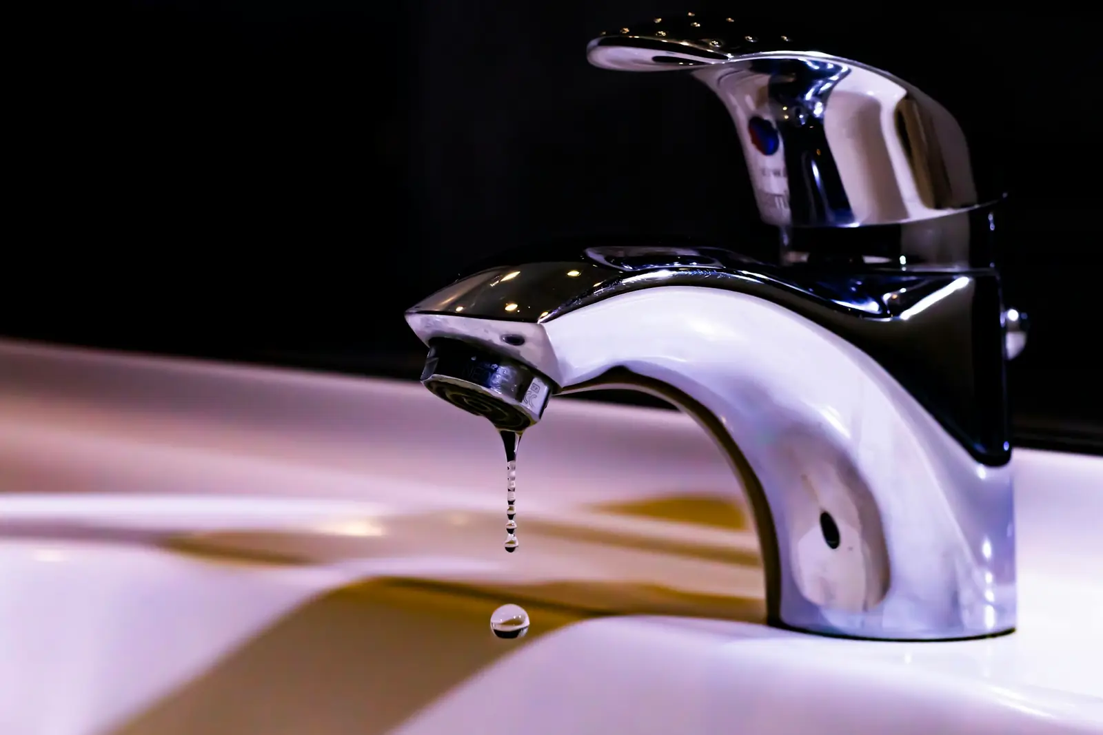 Chrome basin mixer tap dripping water into a white sink
