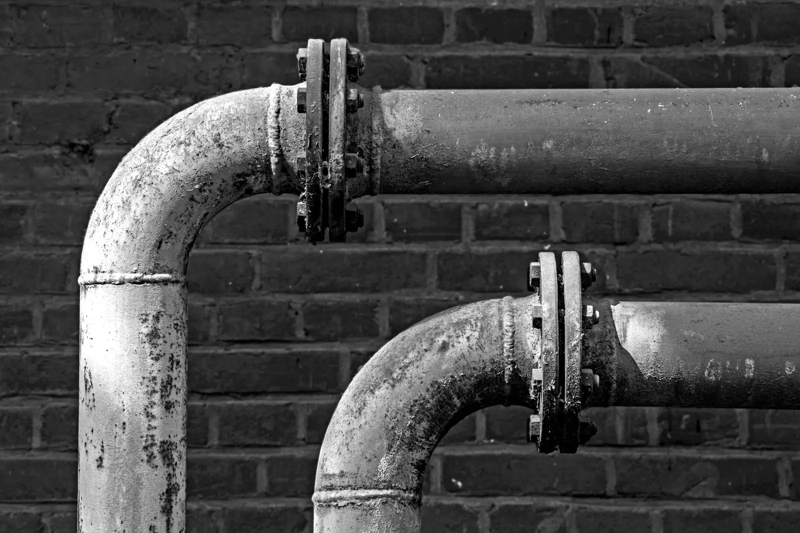 Metal pipes with bends and flanges running along a brick wall