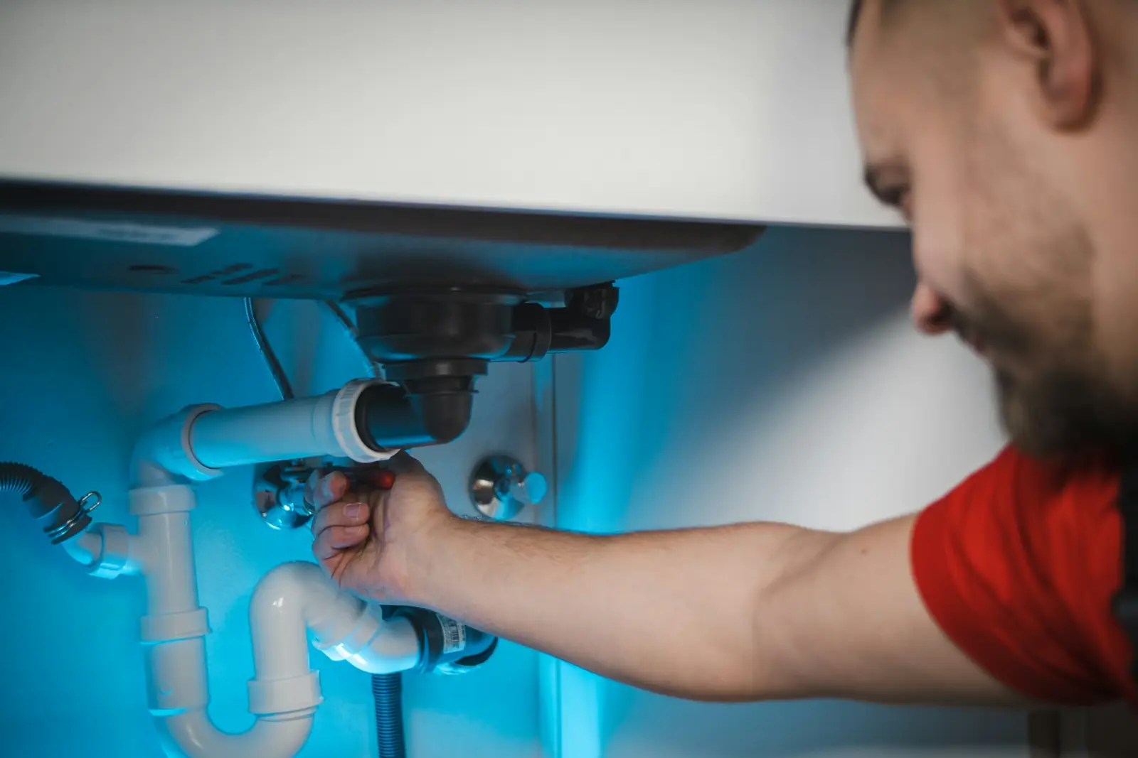 Plumber reaching under a basin to tighten the waste trap and pipework