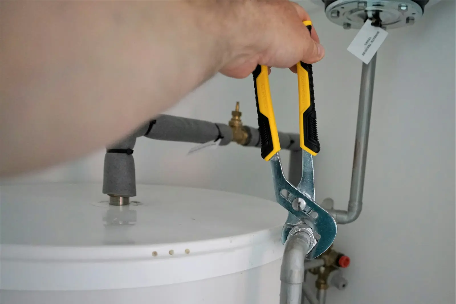 Plumber using a pipe wrench on the connections above a hot water cylinder